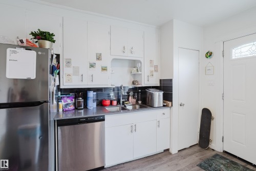 White cabinetry, stainless steel appliances, dark tile backsplash, wood-finish flooring, and a decorative glass panel entry door - 11134 11138 116 Street Nw, Edmonton, AB 