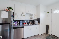 White cabinetry, stainless steel appliances, dark tile backsplash, wood-finish flooring, and a decorative glass panel entry door - 