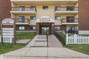 Building exterior with a brick and stucco facade, multiple private balconies, a ground-level patio, a covered main entrance, and a white picket fence - #115 10511 19 Av Nw, Edmonton, AB 
