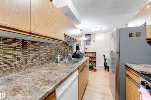 Kitchen featuring wood-finish cabinetry, a mosaic tile backsplash, a stainless steel sink, and wood-finish flooring - #101 49 Akins Dr, St. Albert, AB 