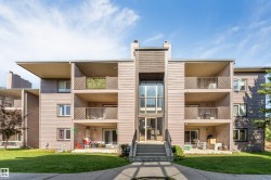 Multi-story building with horizontal siding, multiple balconies with metal railings, a central glass-enclosed entry, and an exterior staircase - 