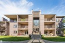 Multi-story building with horizontal siding, multiple balconies with metal railings, a central glass-enclosed entry, and an exterior staircase - #101 49 Akins Dr, St. Albert, AB 