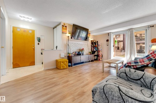 Wood-finish flooring throughout, white painted walls, white brick-style fireplace surround, and a glass sliding door - #101 49 Akins Dr, St. Albert, AB 