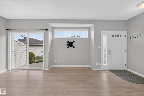 Light-toned wood-finish flooring, sliding glass patio door, transom window, and a white entry door with a clear glass sidelight - #156 460 Cranberry Wy, Sherwood Park, AB 