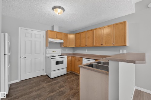 Kitchen featuring wood-finish cabinetry, a double basin stainless steel sink, a built-in dishwasher, and wood-finish flooring - #156 460 Cranberry Wy, Sherwood Park, AB 