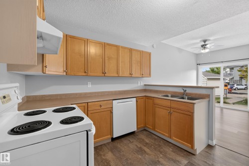 Kitchen featuring wood-finish cabinetry, white appliances, dual basin sink, and wood-finish flooring - #156 460 Cranberry Wy, Sherwood Park, AB 