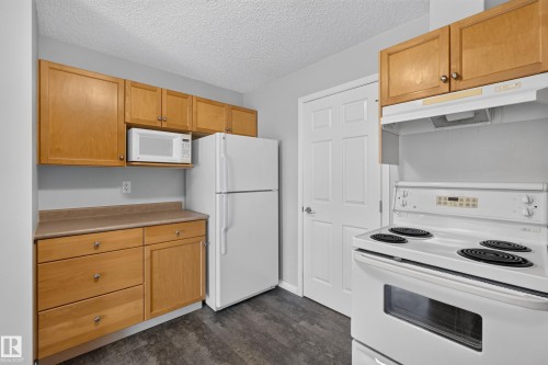 Kitchen featuring wood-finish cabinetry, solid surface countertops, a white electric range, and a white refrigerator - #156 460 Cranberry Wy, Sherwood Park, AB 