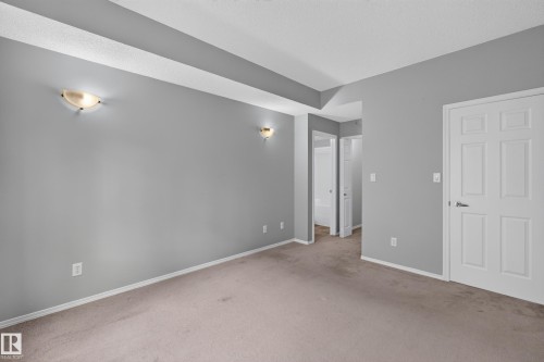 Neutral wall color, wall-mounted sconce lighting, white trim, paneled interior door, and carpeted flooring - #156 460 Cranberry Wy, Sherwood Park, AB 