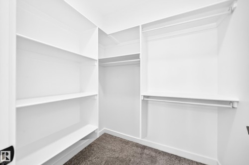 Walk-in closet featuring white built-in shelving, multiple hanging rods, and carpet flooring - 19 Tuplet Bay, Spruce Grove, AB 