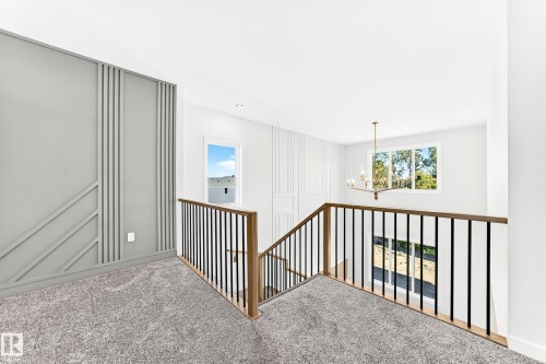 Carpeted landing with decorative wall paneling, a chandelier, and a wood and metal baluster railing - 19 Tuplet Bay, Spruce Grove, AB 