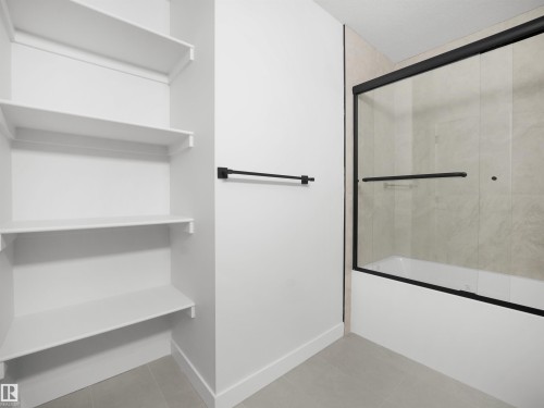 Built-in shelving, black-framed sliding shower doors, integrated bathtub, tiled shower surround, and a matte black towel bar - 12C Twin Terrace Nw, Edmonton, AB 