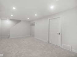 Recessed lighting, light gray carpeting, white walls, white trim, and a white interior door with matte black hardware - 