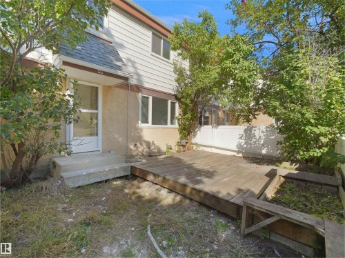 Two-story exterior with light-colored siding, a front entry door with storm door, concrete steps, and a wood deck - 12C Twin Terrace Nw, Edmonton, AB 