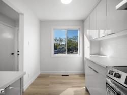 White flat-panel cabinetry with linear pulls, light-toned wood-finish flooring, white countertop, and white subway tile backsplash - 