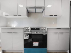 Modern kitchen featuring white flat-panel cabinetry, white tile backsplash, a stainless steel range, and a matching stainless steel range hood - 