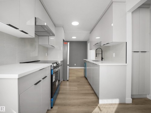 Galley kitchen featuring light-toned cabinetry, stainless steel appliances, wood-finish flooring, and a tiled backsplash - 12C Twin Terrace Nw, Edmonton, AB 