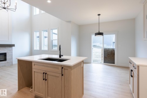 Kitchen island with light wood-finish cabinetry, white countertop, and integrated black sink - 4005 36 Street, Beaumont, AB 