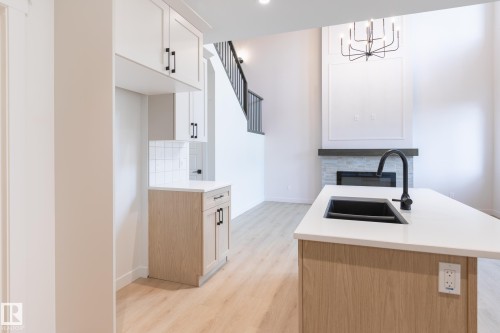 Open-concept living space with wood-finish flooring, a kitchen island featuring a black sink and faucet, white cabinetry, and a fireplace with a stone surround - 4005 36 Street, Beaumont, AB 