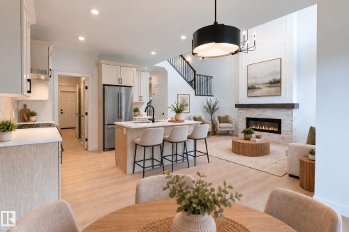 Open-concept living space featuring wood-finish flooring, a kitchen island with seating, a built-in fireplace with a stone surround, and an open staircase with dark railings - 4005 36 Street, Beaumont, AB 
