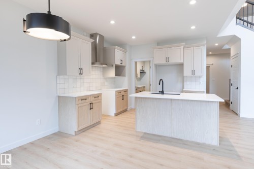 Kitchen featuring light wood-finish flooring, white cabinetry, a kitchen island with a dark faucet, a tiled backsplash, and recessed lighting - 4005 36 Street, Beaumont, AB 