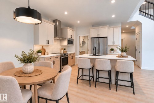 Open-concept kitchen with light wood-finish flooring, white cabinetry, stainless steel appliances, and a central island with a sink - 4005 36 Street, Beaumont, AB 