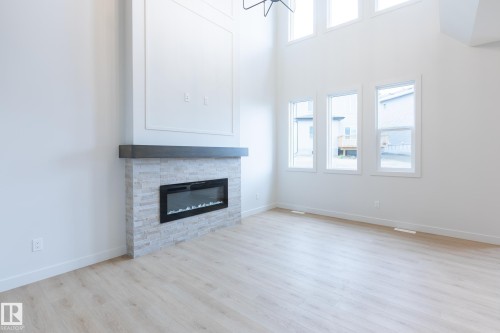 Two-story great room with light wood-finish flooring, a contemporary fireplace with a stone surround, an integrated electric firebox, and a dark mantel - 4005 36 Street, Beaumont, AB 