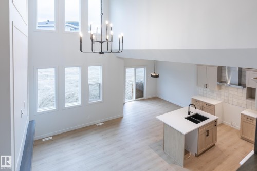 Two-story high ceilings, expansive windows, light wood-finish flooring, central kitchen island with integrated sink, and modern cabinetry - 4005 36 Street, Beaumont, AB 
