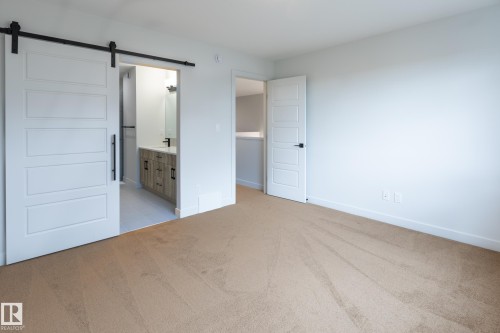 White paneled barn door with black hardware, light neutral carpeting, white interior doors with black hardware, light-toned vanity with black faucet, and a wall-mounted mirror - 4005 36 Street, Beaumont, AB 