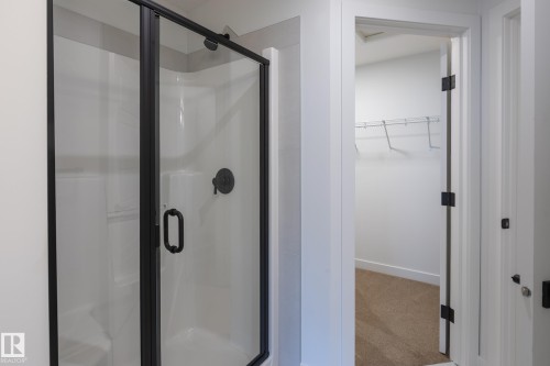 Shower enclosure with matte black hardware and a white shower base, featuring a neutral tone carpeted closet with wire shelving - 4005 36 Street, Beaumont, AB 