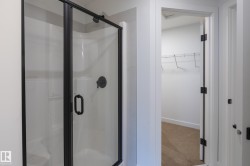 Shower enclosure with matte black hardware and a white shower base, featuring a neutral tone carpeted closet with wire shelving - 