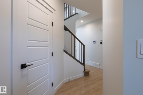 Modern four-panel interior door with matte black hardware, wood-finish flooring, and staircase with dark wood handrail and black metal spindles - 4005 36 Street, Beaumont, AB 
