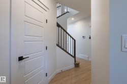 Modern four-panel interior door with matte black hardware, wood-finish flooring, and staircase with dark wood handrail and black metal spindles - 