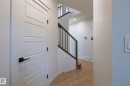 Modern four-panel interior door with matte black hardware, wood-finish flooring, and staircase with dark wood handrail and black metal spindles - 4005 36 Street, Beaumont, AB 