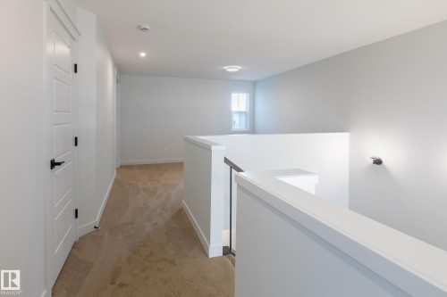 Loft area featuring neutral carpet flooring, a white interior door with black hardware, and a white railing with black balusters - 4005 36 Street, Beaumont, AB 