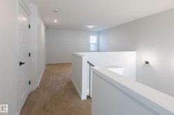 Loft area featuring neutral carpet flooring, a white interior door with black hardware, and a white railing with black balusters - 