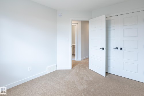 Light-colored carpeting with white trim, modern white doors with matte black hardware, and an adjoining space with recessed lighting - 4005 36 Street, Beaumont, AB 