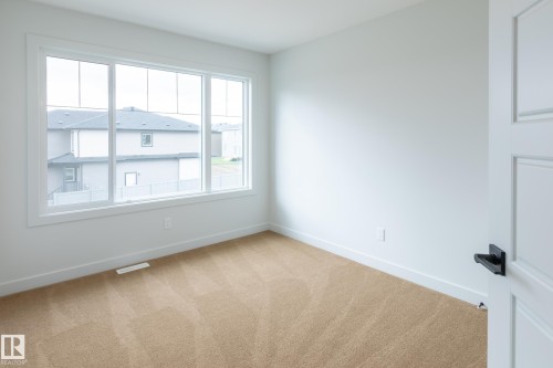 Light-filled interior featuring a large multi-pane window, neutral-toned carpet, white walls, and a paneled door with matte black hardware - 4005 36 Street, Beaumont, AB 
