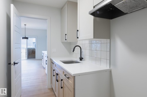White cabinetry with matte black hardware, white subway tile backsplash, stainless steel sink, black gooseneck faucet, and light wood-finish flooring - 4005 36 Street, Beaumont, AB 