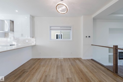 Open-concept living area featuring wood-finish flooring, a contemporary chandelier, and a glass-panel railing - 6047 180 Avenue Nw, Edmonton, AB 