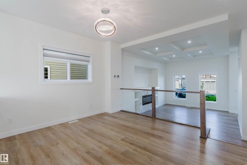 Wood-finish flooring, contemporary chandelier, glass panel railing with wood posts, recessed lighting, and a coffered ceiling - 6047 180 Avenue Nw, Edmonton, AB 