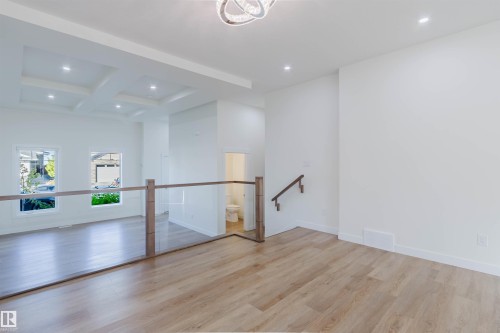 Light wood-finish flooring throughout, bright white walls, contemporary ceiling light fixture, recessed lighting, and a glass-paneled railing with wood newel posts - 6047 180 Avenue Nw, Edmonton, AB 