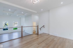 Light wood-finish flooring throughout, bright white walls, contemporary ceiling light fixture, recessed lighting, and a glass-paneled railing with wood newel posts - 