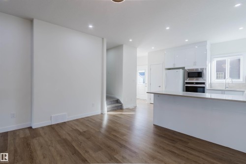 Open-concept kitchen with white cabinetry and integrated appliances, wood-finish flooring, recessed lighting, and a kitchen island with stone countertop - 6047 180 Avenue Nw, Edmonton, AB 