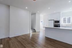 Open-concept kitchen with white cabinetry and integrated appliances, wood-finish flooring, recessed lighting, and a kitchen island with stone countertop - 