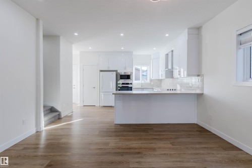 Open-concept kitchen with white cabinetry and appliances, wood-finish flooring, and recessed lighting - 6047 180 Avenue Nw, Edmonton, AB 