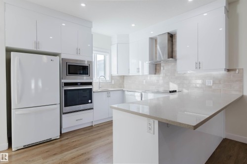 Contemporary kitchen featuring white cabinetry, light-toned countertops, a full suite of appliances, recessed lighting, and wood-finish flooring - 6047 180 Avenue Nw, Edmonton, AB 