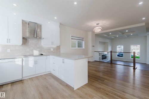 Kitchen featuring white cabinetry, light-toned backsplash, stainless steel range hood, and wood-finish flooring - 6047 180 Avenue Nw, Edmonton, AB 