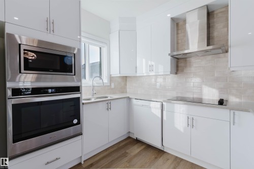 Modern kitchen featuring white cabinetry, stainless steel appliances, light-toned tiled backsplash, and wood-finish flooring - 6047 180 Avenue Nw, Edmonton, AB 