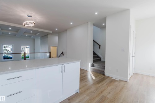 Expansive white kitchen island with a light-toned countertop, wood-finish flooring, recessed lighting, and a coffered ceiling - 6047 180 Avenue Nw, Edmonton, AB 