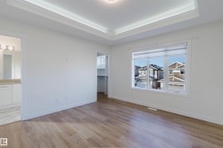 Recessed ceiling with crown molding, wood-finish flooring, white window blinds, built-in shelving, and an en-suite bathroom with a vanity - 